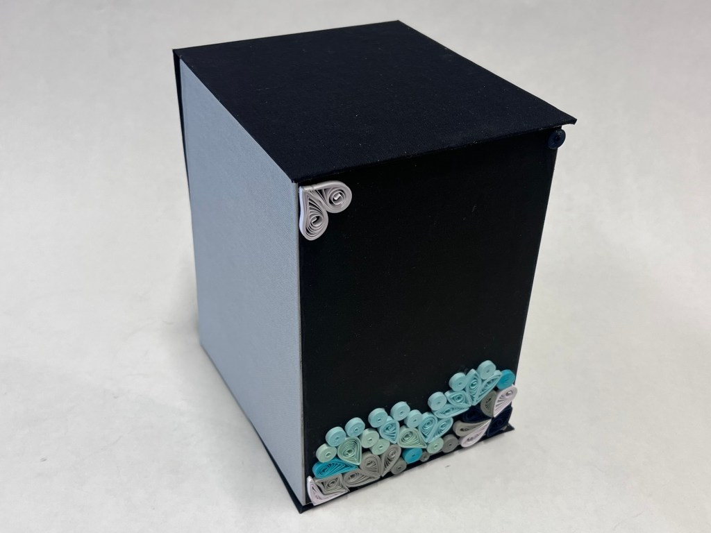 a black large hinged box. it is closed and decorated at the bottom with green paper quilled swirls