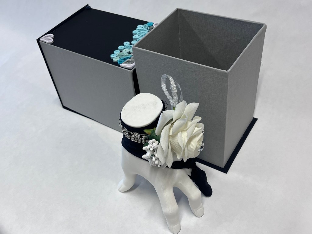 the hand sculpture, wearing a black glove and a white coraage is removed from the large box