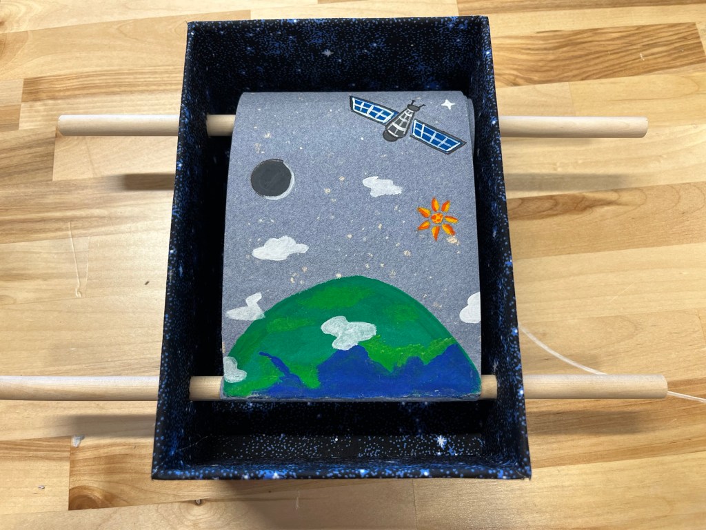 a box scroll book, earch surrounded by a sun, moon, and satelite