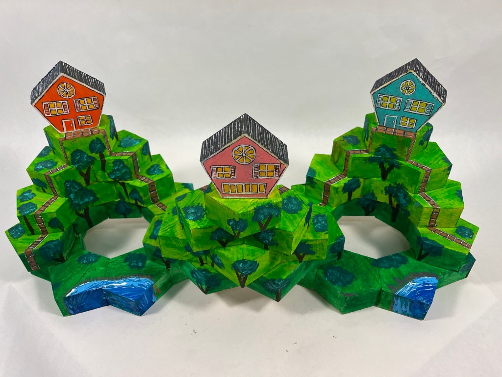 wooden sculpture made of hexagonal shapes, depicting three houses on three hills
