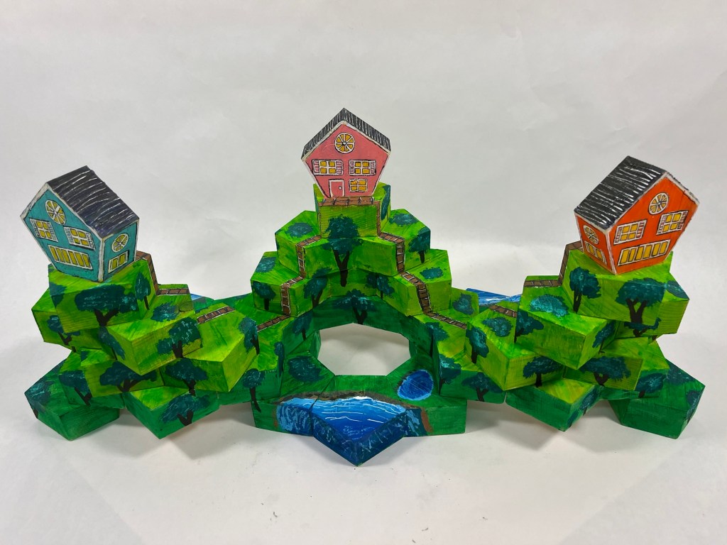 wooden sculpture made of hexagonal shapes, depicting three houses on three hills