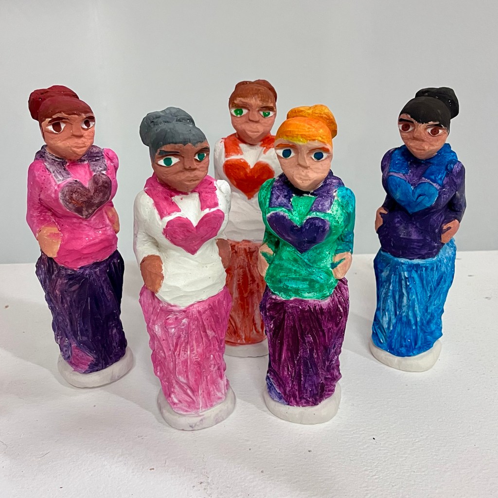 painted plaster sculptures of five women wearing dresses with heart symbols on the front