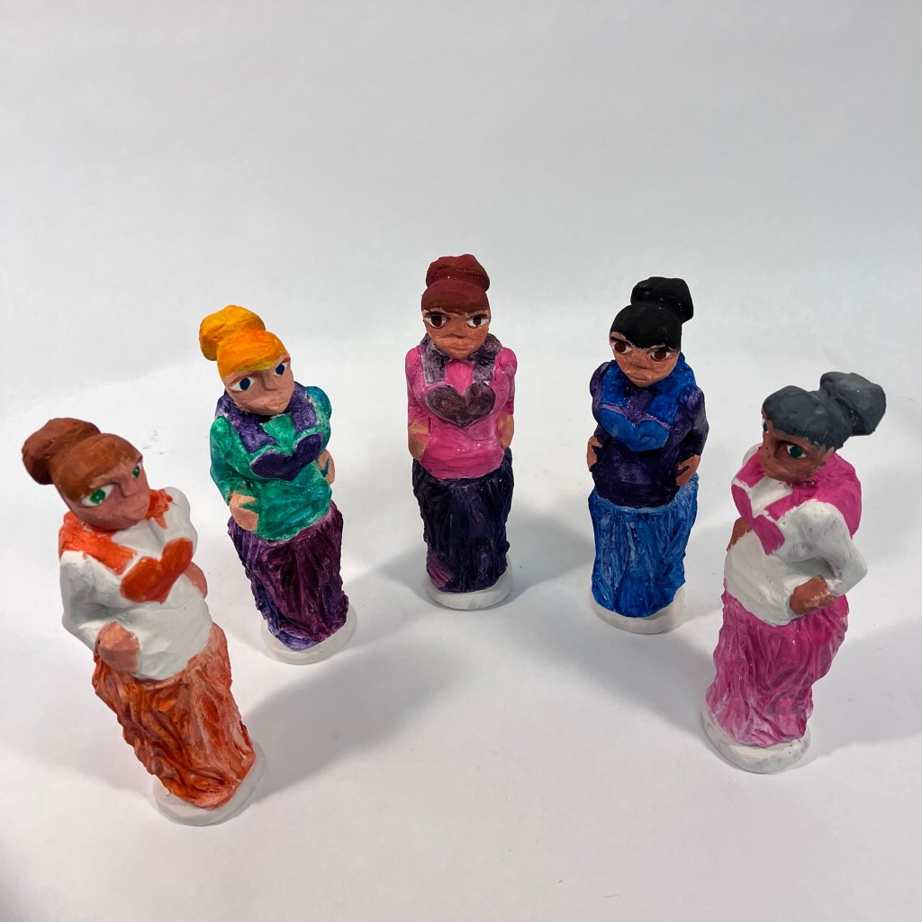 painted plaster sculptures of five women wearing dresses with heart symbols on the front
