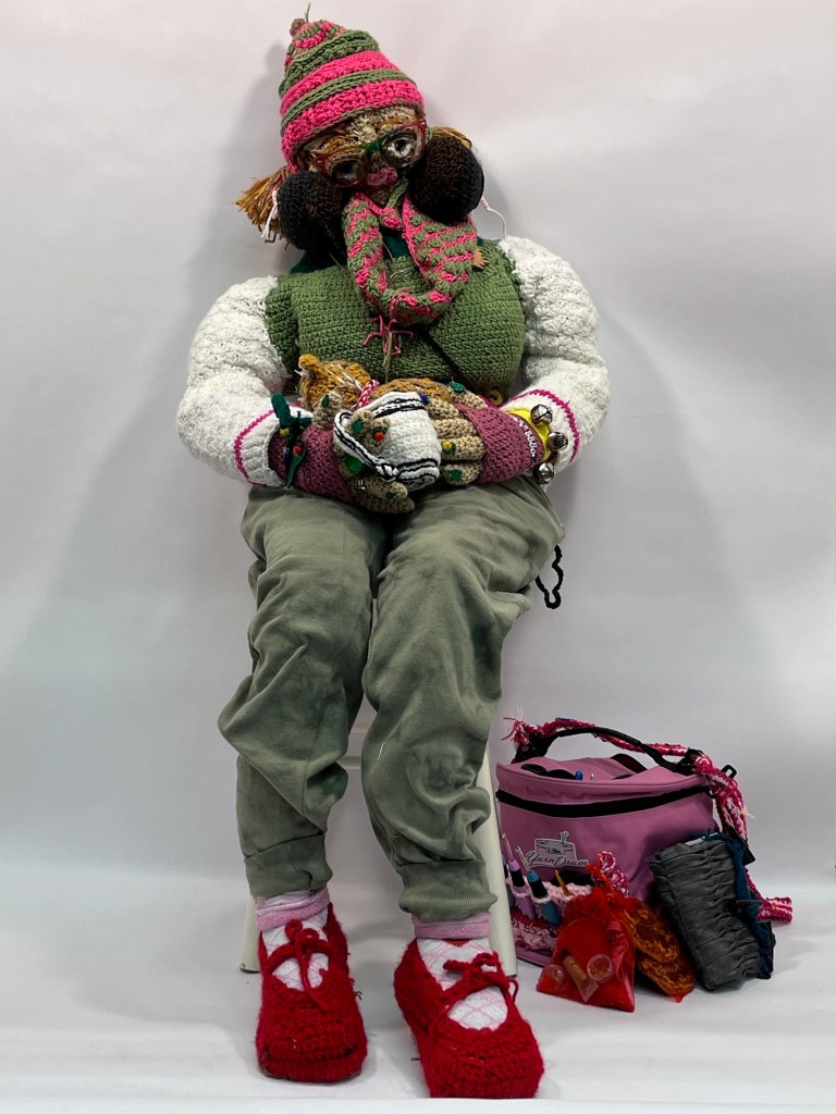 A crocheted self portrait of Sophia holding a coffee cup and a kitten