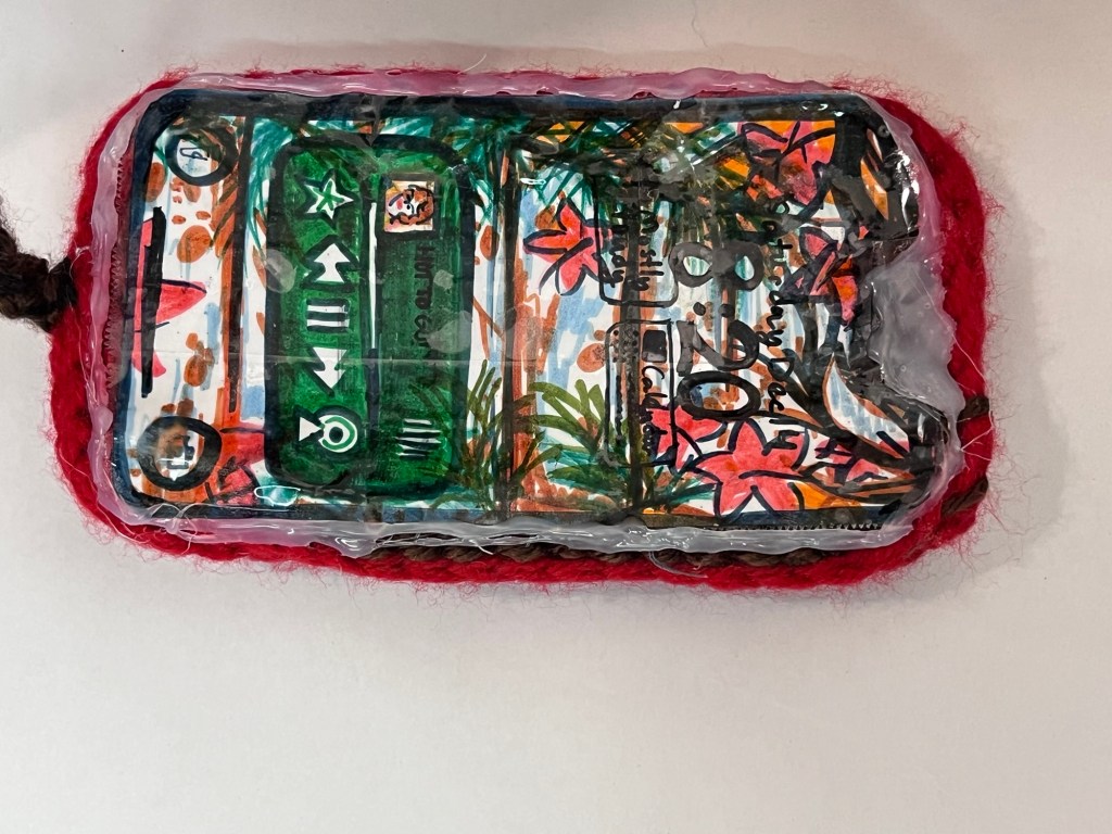 Crocheted Phone Screen, the screen has a marker drawn replica of one of Sophia's winter drawings, a drawing of the music player app shows that there is music playing